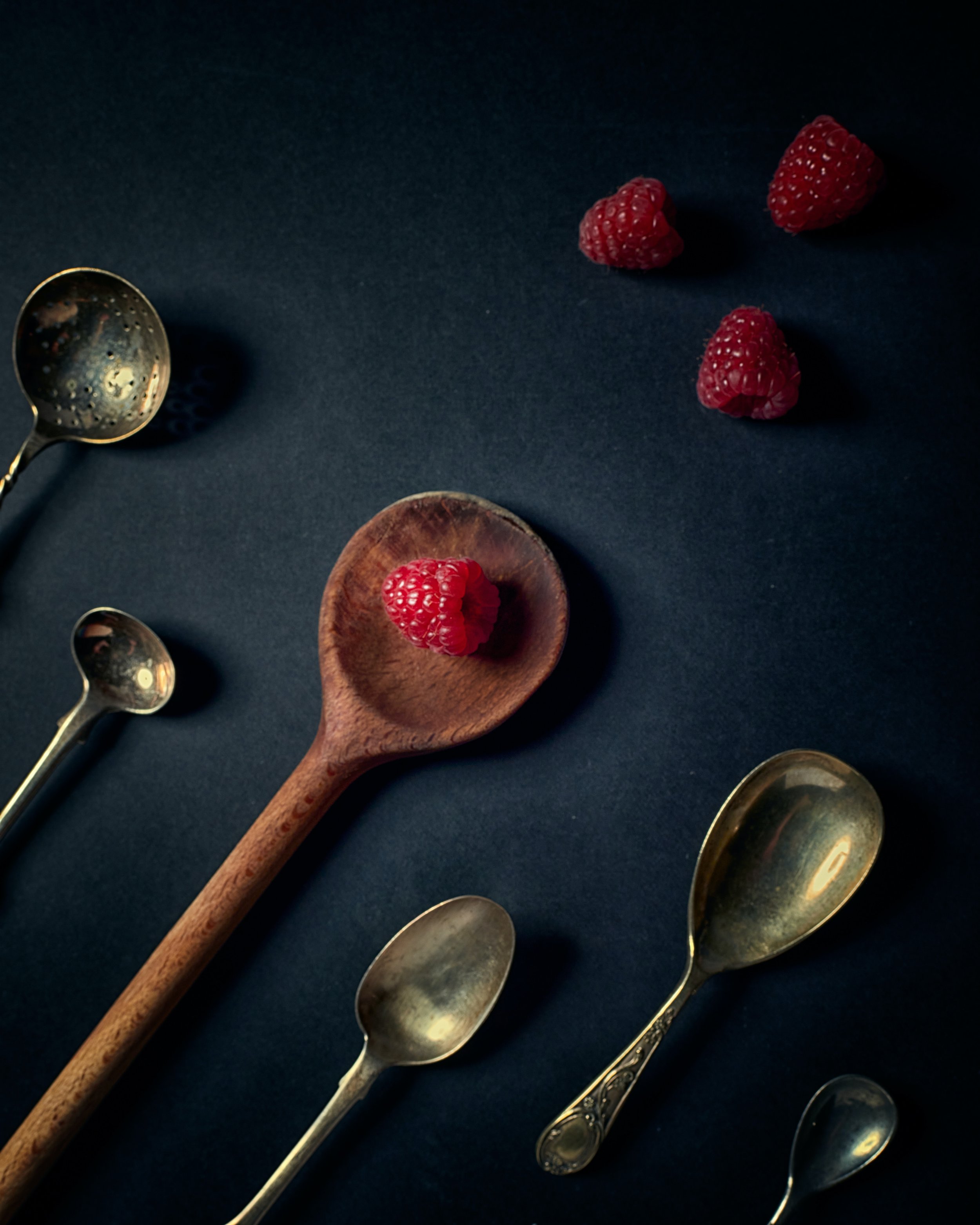 A hand-carved wooden spoon among antique spoons on a deep navy surface