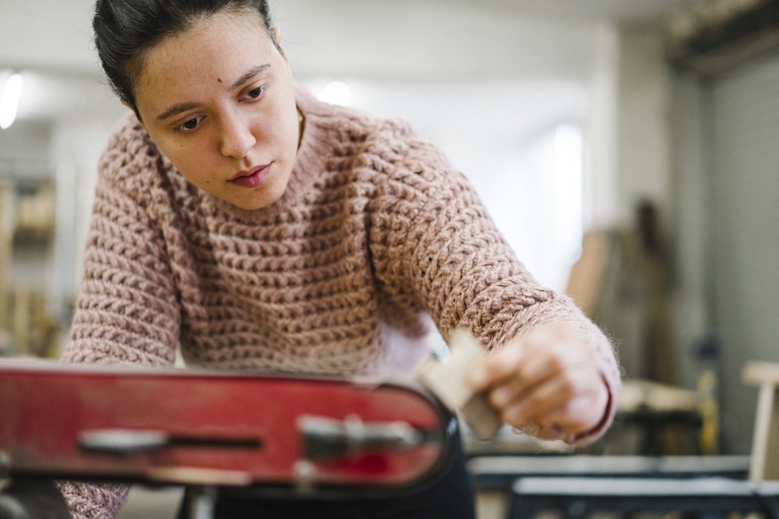 A workshop guest in a pink sweater sanding a wooden piece at the bench